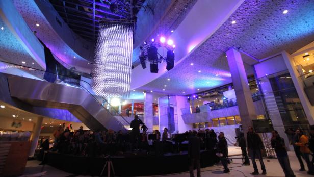 Ein Orchester spielt in einem Einkaufszentrum unter einer großen Lichtinstallation.