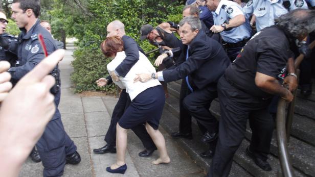 Polizisten führen eine Frau barfuß eine Treppe hinunter.