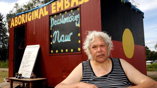 Eine Frau steht vor der Aboriginal Embassy, auf der „Decolonising Now“ geschrieben steht.