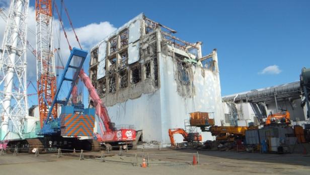 Ein beschädigtes Gebäude in Fukushima wird von mehreren Kränen und Baumaschinen umgeben.