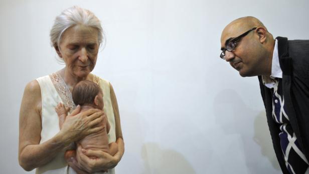 Eine ältere Frau hält ein Baby im Arm, während ein Mann sie aufmerksam betrachtet.