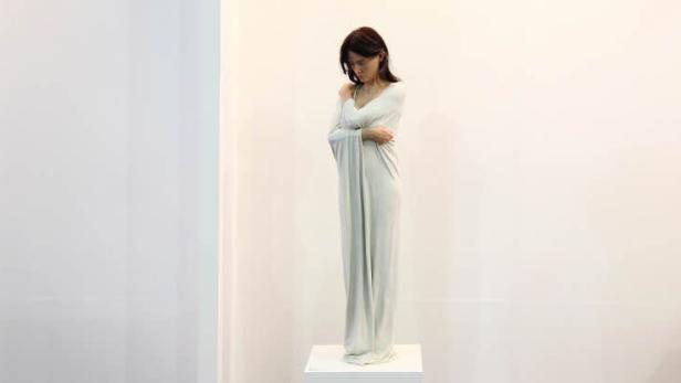 Eine Frau in einem langen, hellen Kleid steht auf einem Sockel.