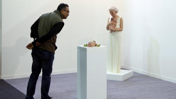 Ein Mann betrachtet eine Skulptur eines Babys auf einem Sockel und eine ältere Frau, die ein Baby hält.