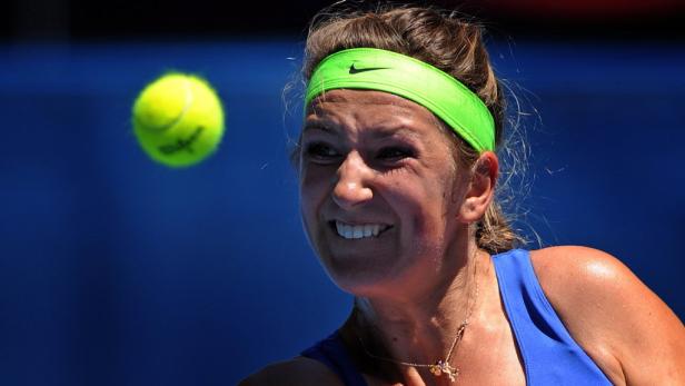 Eine Tennisspielerin mit grünem Stirnband lächelt, während ein Tennisball auf sie zukommt.