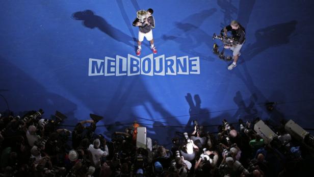 Novak Đoković küsst die Trophäe vor der Kulisse von Melbourne, umringt von Fotografen.