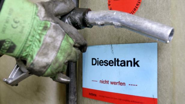 Eine Hand mit Arbeitshandschuh hält einen Zapfhahn vor einem Schild mit der Aufschrift „Dieseltank – nicht werfen“.