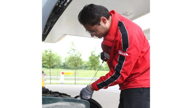 Ein Mann in roter Jacke überprüft den Ölstand eines Autos.