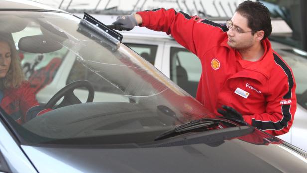 Ein Mann in Shell-Kleidung reinigt die Windschutzscheibe eines Autos.
