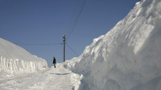 Ein Mann steht auf einer schneebedeckten Straße zwischen hohen Schneewänden.