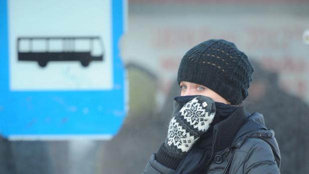 Eine Frau mit Mütze und Handschuhen wartet an einer Bushaltestelle.