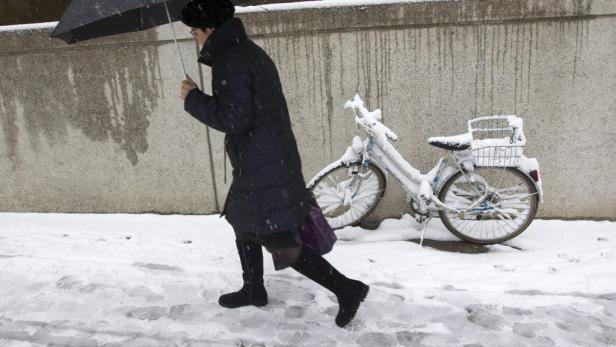 Eine Frau geht mit einem Regenschirm im Schnee an einem schneebedeckten Fahrrad vorbei.