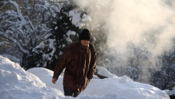 Ein Mann mit Mütze und Jacke geht durch eine verschneite Landschaft.