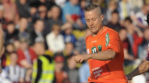 Ein Fußballspieler in einem orangefarbenen Trikot auf dem Spielfeld.