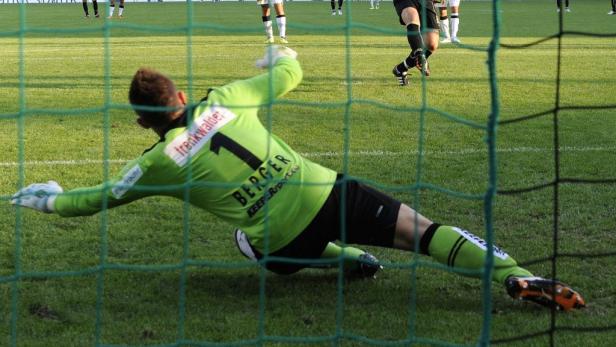 Ein Torwart in grüner Uniform hechtet nach dem Ball.