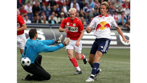 Ein Fußballspieler schießt auf das Tor, während der Torwart versucht, den Ball abzuwehren.