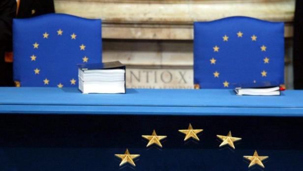 Zwei Stühle mit der EU-Flagge und Dokumente auf einem Tisch.