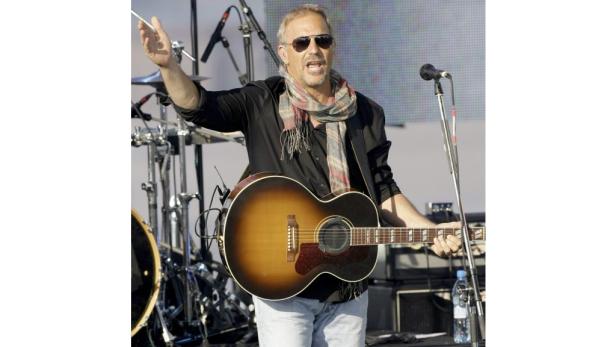 Kevin Costner spielt Gitarre auf einer Bühne.