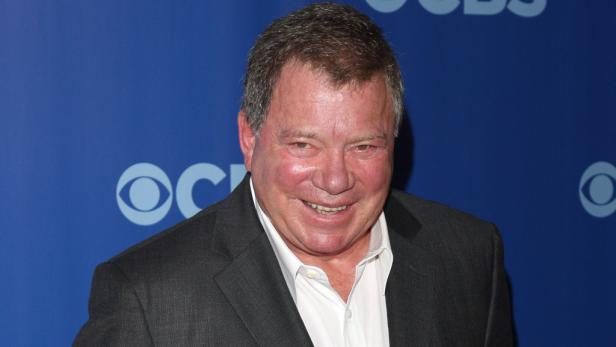William Shatner lächelt vor einem blauen Hintergrund mit dem CBS-Logo.