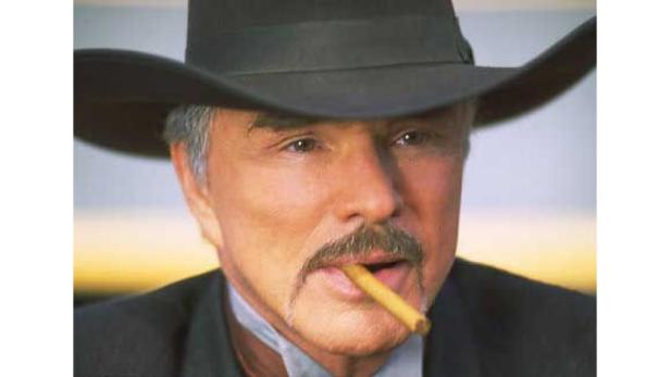 Burt Reynolds mit Cowboyhut und Zigarre im Mund.