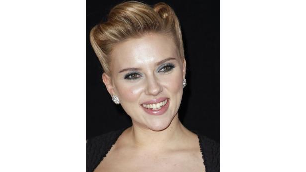 Scarlett Johansson lächelt mit hochgesteckten blonden Haaren und Ohrringen.