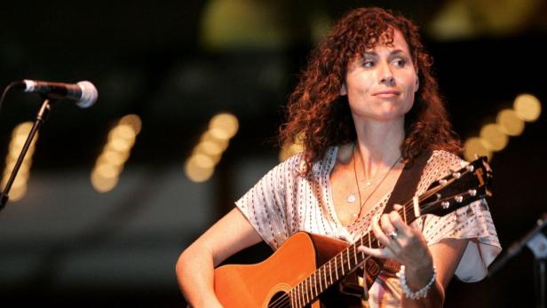 Eine Frau mit lockigem Haar spielt Gitarre auf einer Bühne.