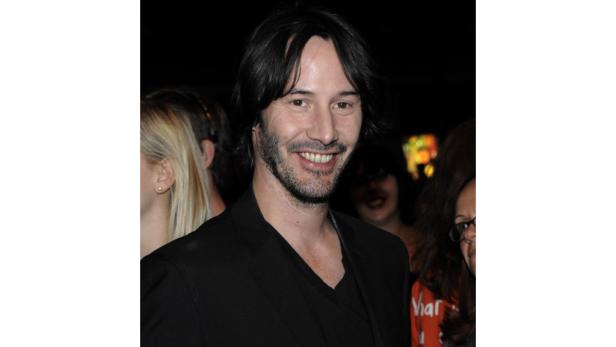 Keanu Reeves lächelt in einem schwarzen Anzug.