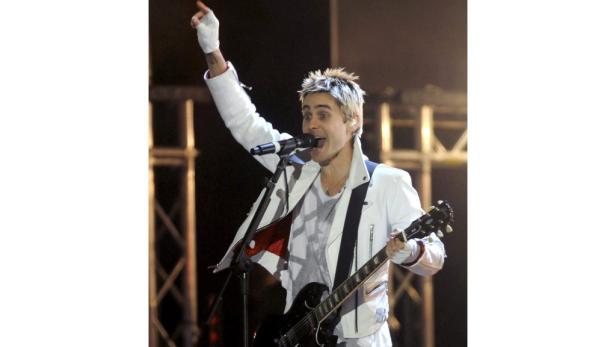 Jared Leto tritt mit Gitarre und erhobenem Arm auf einer Bühne auf.