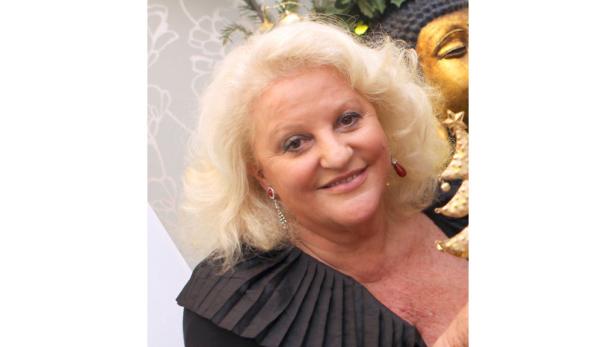 Eine Frau mit blonden Locken und Ohrringen lächelt in die Kamera.