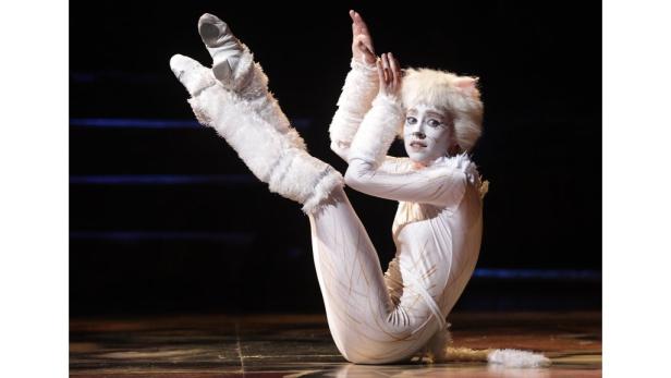 Eine Darstellerin in einem weißen Katzenkostüm auf einer Bühne.