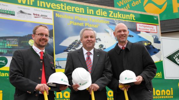 Drei Männer halten Bauhelme vor einem Schild für den Neubau der Planai Talstation „Planet Planai“.