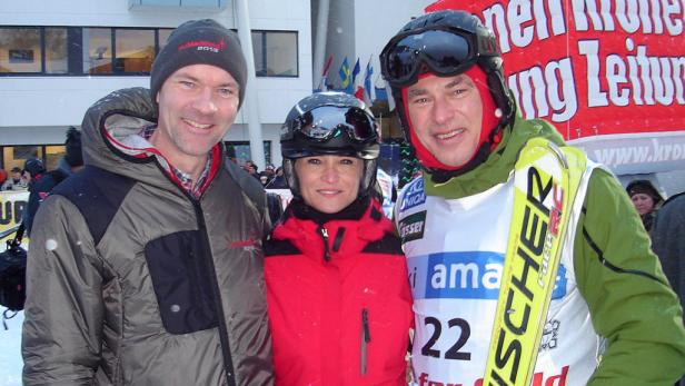 Drei Personen in Winterkleidung stehen zusammen, eine davon mit Skiern.