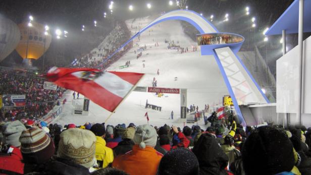Ein Skirennen bei Nacht mit Zuschauern und einer österreichischen Flagge.