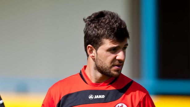 Ein Mann mit kurzem, dunklem Haar und Bart trägt ein rotes Sporttrikot.