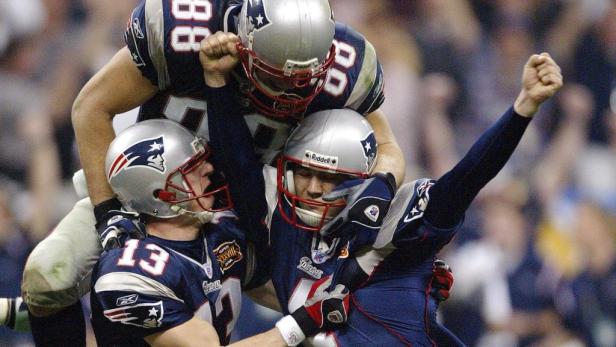 Jubelnde Footballspieler der New England Patriots umarmen sich auf dem Spielfeld.