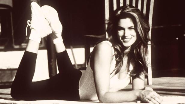 Cindy Crawford liegt auf dem Bauch und lächelt in die Kamera.