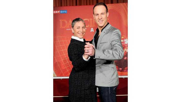 Ein Mann und eine Frau posieren vor einem roten „Dancing Stars“-Hintergrund.