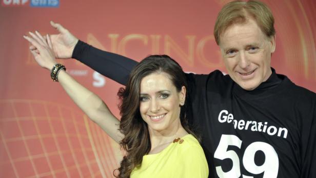 Ein Mann und eine Frau posieren lächelnd vor einem roten Hintergrund.