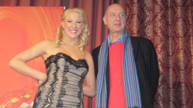 Eine blonde Frau in einem Kleid posiert mit einem Mann vor einem roten Vorhang.