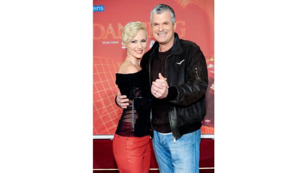 Ein Mann und eine Frau posieren vor einem roten Hintergrund für ein Foto.