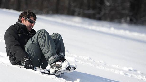 Ein Mann mit Sonnenbrille fährt auf einem Schlitten einen schneebedeckten Hügel hinunter.