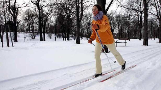 Eine Frau läuft im Winter auf Skiern durch einen Park.