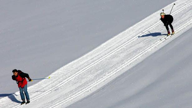 Zwei Personen laufen auf einer schneebedeckten Loipe Ski.