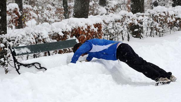Eine Person macht Liegestütze im Schnee neben einer Parkbank.