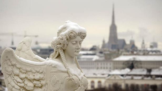 Eine geflügelte Frauenskulptur mit schneebedecktem Kopf vor der Skyline von Wien.