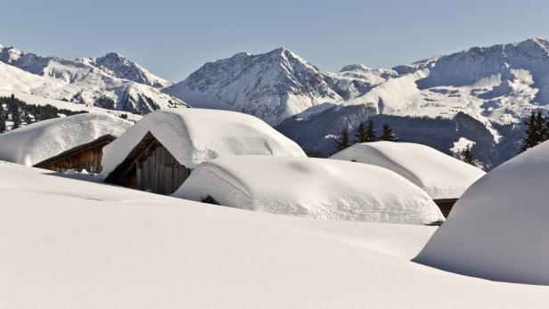 Verschneite Holzhütten vor einer Bergkulisse.