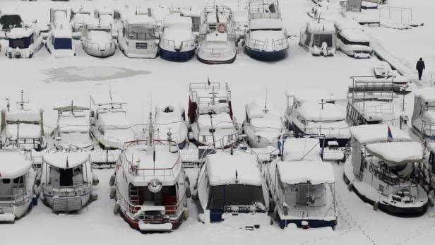 Viele schneebedeckte Boote liegen in einem Hafen vor Anker.