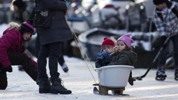 Zwei Kinder sitzen in einer Wanne, die als Schlitten auf dem Eis gezogen wird.