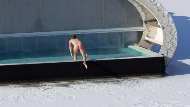 Eine unbekleidete Person steigt in ein Schwimmbecken im Schnee.