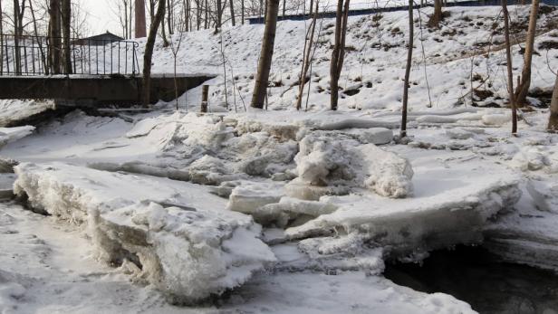 Ein zugefrorener Bach unter einer Brücke im Winter.