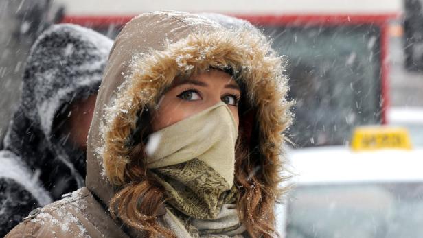 Eine Frau mit Kapuze und Schal steht im Schneefall.